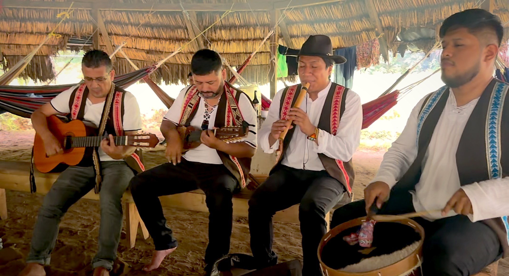 Four musicians playing guitar, tiple, flute and drum together under the thatched roof of the ceremony house