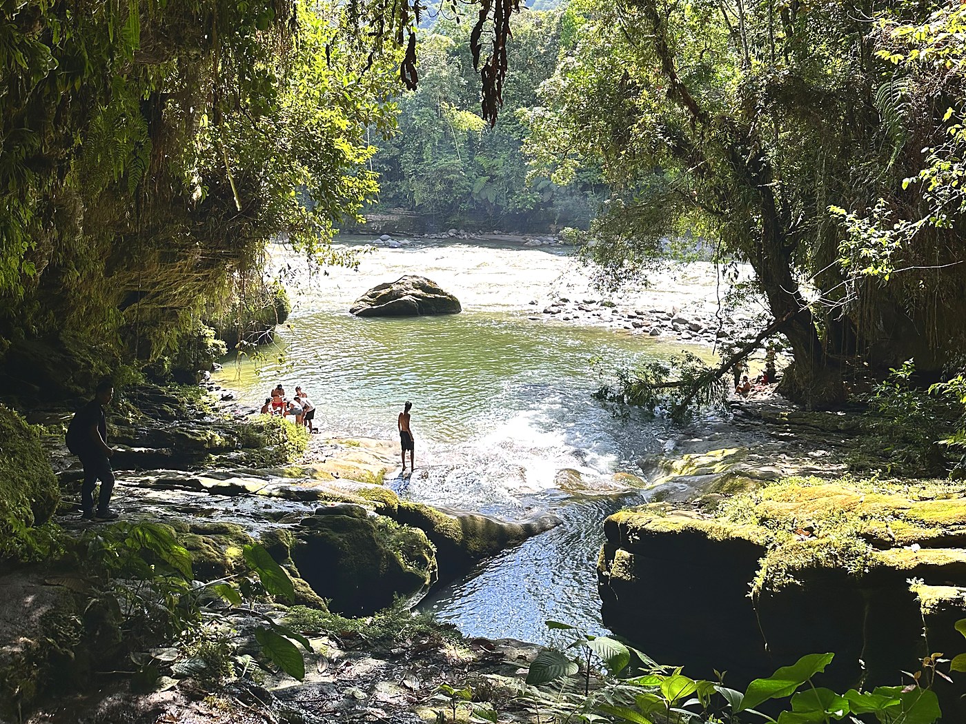 Guests bathing in a river pool below mossy jungle rocks